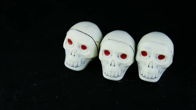 human hand put three white chocolate candies in skeleton skull shape with red eyes on black background