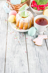 Easter table setting concept, festive table with decoration of young grass, cake, pastel colored eggs, homemade cookies in shape of eggs, bunny rabbits. On a wooden background, copy space