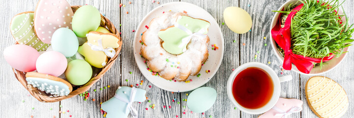 Easter table setting concept, festive table with decoration of young grass, cake, pastel colored eggs, homemade cookies in shape of eggs, bunny rabbits. On a wooden background, copy space banner
