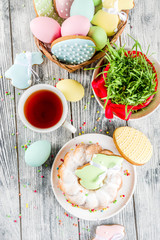 Easter table setting concept, festive table with decoration of young grass, cake, pastel colored eggs, homemade cookies in shape of eggs, bunny rabbits. On a wooden background, copy space