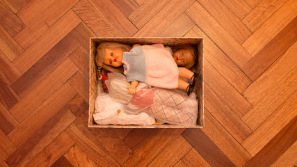 Central open box on a wooden floor full with collectible vintage dolls with warm and smooth lighting in a house interior. Childhood collections concept