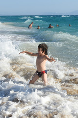 Happy little boy playing on the beach. Child run and play with waves on beach