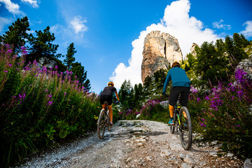 Cycling woman and man riding on bikes in Dolomites mountains landscape. Couple cycling MTB enduro trail track. Outdoor sport activity.