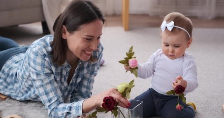 Cute baby girl with mother smelling and inserting rose flowers in vase