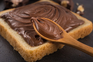 Chocolate spread on slice of bread with spoon, melted cream white bowl