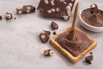 Chocolate spread on slice of bread with spoon, melted cream white bowl