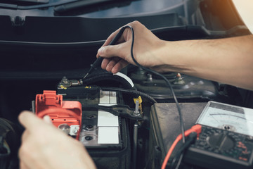 Close up car mechanic is using the car battery meter to measure various values and analyze it.