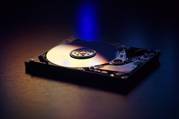 Open / disassembled hard disk on the table in dark colors and lights close-up. Selective soft focus.