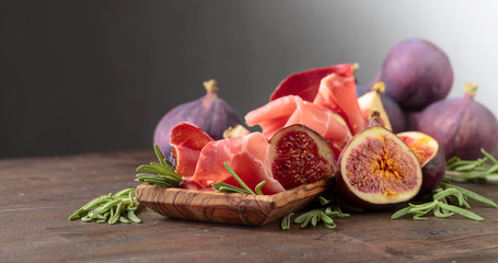 Prosciutto with figs and rosemary on a old wooden table.