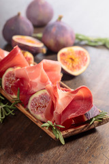 Prosciutto with figs and rosemary on a old wooden table.