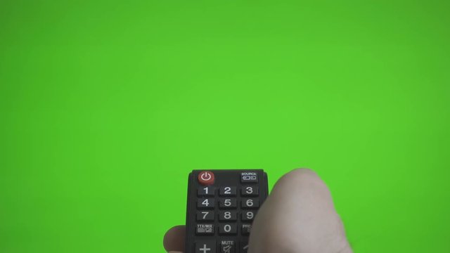 Male hand with remote control turns on the TV over green screen. Place for your advertisement.