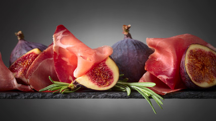 Prosciutto with figs and rosemary on a dark background.