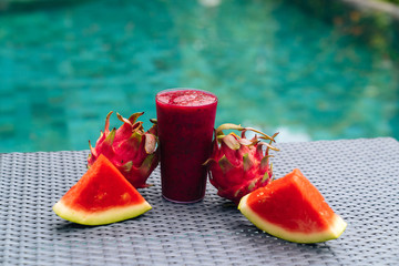 Close up glass of dragon fruit smoothie and two slices of juicy watermelon on textured table with...