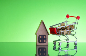 Shopping cart, Coins and house box on green background. Business and Finance concept. Selective...