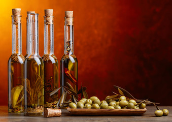 Green olives and bottles of olive oil with spices and herbs.