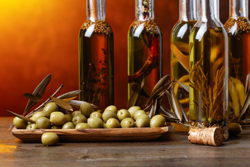 Green olives and bottles of olive oil with spices and herbs .