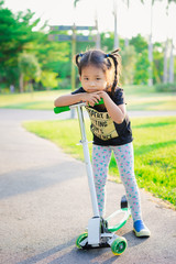 Cute little asian girl learning to ride a scooter in a park