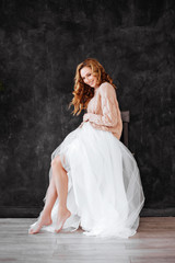 Fototapeta premium Studio shot of beautiful young woman with blonde hair wearing loose long-sleeved sweater over white dress. Beauty and youth