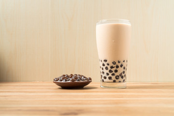 A glass cup of pearl milk tea (also called bubble tea) and a plate of tapioca ball on wooden background. Pearl milk tea is the most representative drink in Taiwan. Taiwan food . With copy space.