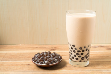 A glass cup of pearl milk tea (also called bubble tea) and a plate of tapioca ball on wooden background. Pearl milk tea is the most representative drink in Taiwan. Taiwan food . With copy space.