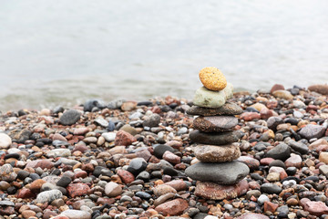 A pyramid of stones with a bright stone at the top stands on the sandy beach. The concept of leadership