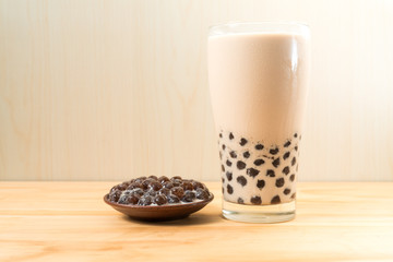 A glass cup of pearl milk tea (also called bubble tea) and a plate of tapioca ball on wooden background. Pearl milk tea is the most representative drink in Taiwan. Taiwan food . With copy space.