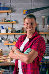 Smiling locksmith is standing in the workshop against the background of a wall with shelves for tools