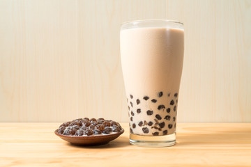 A glass cup of pearl milk tea (also called bubble tea) and a plate of tapioca ball on wooden background. Pearl milk tea is the most representative drink in Taiwan. Taiwan food . With copy space.