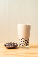 A glass cup of pearl milk tea (also called bubble tea) and a plate of tapioca ball on wooden background. Pearl milk tea is the most representative drink in Taiwan. Taiwan food . With copy space.