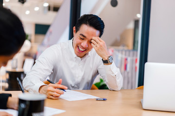 A youthful Asian Chinese expert is giving an introduction before his colleague in the workplace. He is exceptionally content with the discussion and looking brilliant in his office clothing.