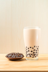 A glass cup of pearl milk tea (also called bubble tea) and a plate of tapioca ball on wooden background. Pearl milk tea is the most representative drink in Taiwan. Taiwan food . With copy space.