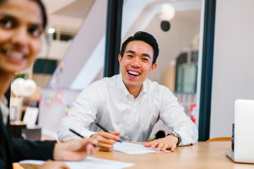 A youthful Asian Chinese expert is giving an introduction before his colleague in the workplace. He is exceptionally content with the discussion and looking brilliant in his office clothing.