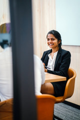 A lovely Indian lady sitting next to a partner inside a conference room. She is discussing some strategy regarding a room and looking pretty in her office attire.