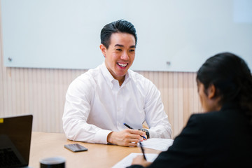A young Asian Chinese professional is giving a presentation in front of his teammate in the office. He is very happy with the talk and looking very smart in his office attire.