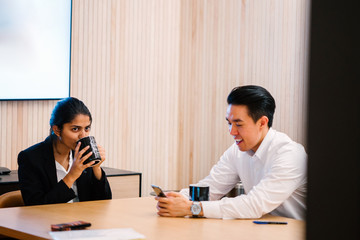 Teammate talking to each other while enjoying their coffee. They are discussing work-related stuff inside a conference room and looking good in their office attire.