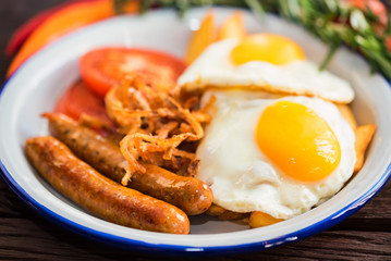 Typial breakfast with eggs, tomato, onion rings and sausage on plate