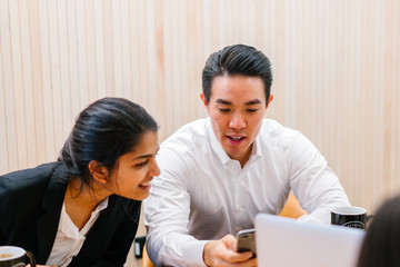 A Chinese Asian manager is showing his cellular phone with his officemate in a meeting room. He is...