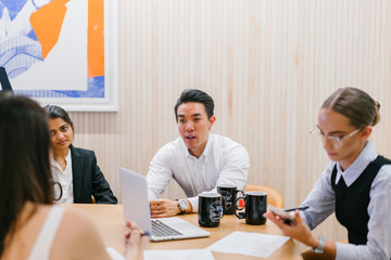 A diverse team sitting around a table for a business discussion in a meeting room in the office. They are ethnically diverse and includes an Indian, Caucasian and Eurasian woman and a Chinese man.