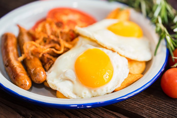 Typial breakfast with eggs, tomato, onion rings and sausage on plate