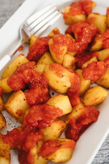 Papas Bravas, deep fried potato cubes typically served as tapas in Madrid, Spain with spicy mojo rojo, a red hot sauce made of tomatoes, bell peppers, onions and chili on white plate and wooden table