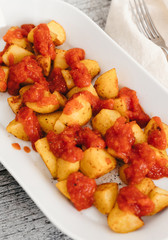 Patatas Bravas, oven-baked potato cubes traditionally served as tapas in Spain with spicy mojo rojo, a red hot salsa made of tomatoes, bell peppers, onions and chile on white plate  and wooden table