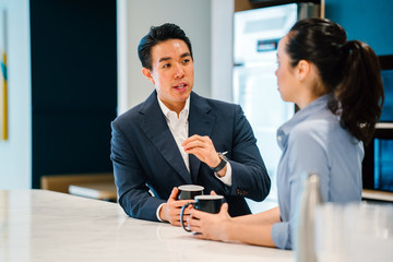 An Asian Chinese man in a suit having a discussion with his Asian woman colleague in an office...