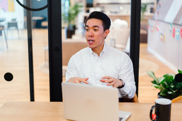 An attractive Chinese Asian man sits on a chair and stops for a moment to talk with his group amid...