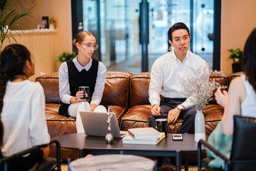 A group of professionals discussing work inside the office. They are wearing elegant corporate attire while sitting on a brown couch. 