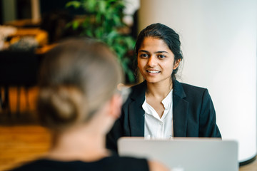 A lovely Indian lady sitting by an accessory inside a cafeteria. She is telling a joke with a...