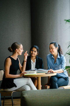 A young Caucasian woman is having a casual business meeting with her team in a meeting room. They are sitting and having an animated conversation. The team is diverse (Indian and Chinese). 