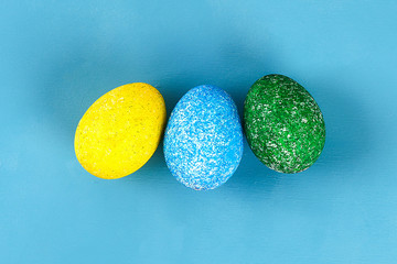 Diy Easter egg painted with colored rice on a blue background. The decor of eggs for Easter