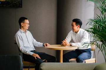 Portrait of two Chinese entrepreneurs sitting at a table. They are smiling as they smile and talk...