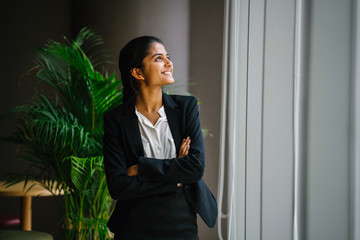 Portrait of a young Indian Asian businesswoman standing by the window in a meeting room, smiling...