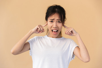 Portrait of irritated asian woman wearing basic t-shirt plugging ears with her fingers